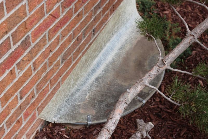 Covered basement window well beside a house foundation