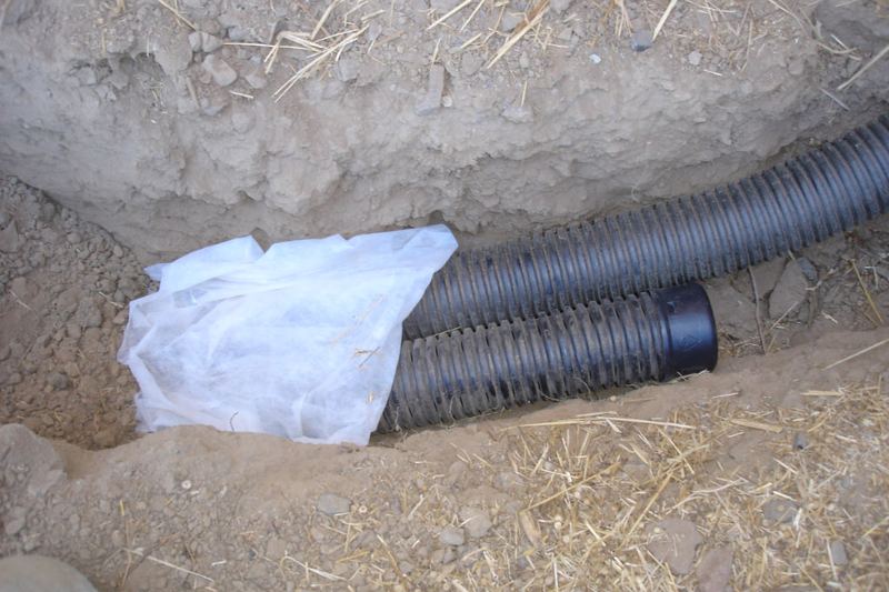 Perforated drain pipe laid on gravel in a French drain trench